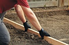 a man in red shirt and black pants working on a garden bed with wooden boards