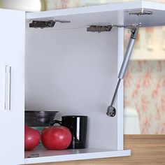 an open cabinet with apples and cups on it