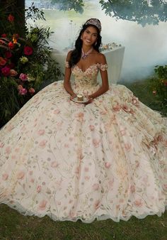 Embrace your inner fairytale princess with this whimsical Vizcaya quinceaera ball gown (style 89457). The delicately draped bodice features classic off-the-shoulder sleeves accented by stunning crystal beaded, three-dimensional flowers that add a touch of whimsy. The real magic lies in the skirt, crafted with a stunning combination of floral printed tulle layered over luxurious sparkle tulle. This creates a dimensional effect that shimmers with every move. Pickups in the skirt create a cascading waterfall look, further adding to the whimsical feel. Three-dimensional flowers are scattered throughout the skirt, echoing the details on the bodice and tying the whole look together. To complete your regal presence, a matching stole is included. This dress is sure to make you feel like a quinceae Cascading Waterfall, Allure Couture, Quinceanera Themes, Quince Dress, Sherri Hill Prom Dresses, Theme Dress, Mori Lee