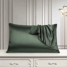 a green satin pillow on a white dresser