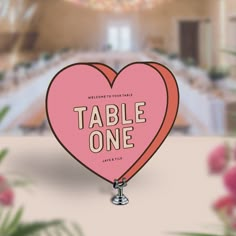 a pink heart shaped sign with the words table one on it