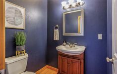 a bathroom with blue walls and white fixtures, including a sink, toilet and mirror