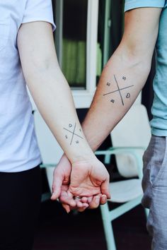 two people holding hands with tattoos on their arms