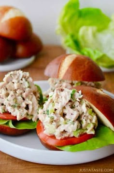 two sandwiches with chicken salad on them sit on a plate next to lettuce and tomatoes