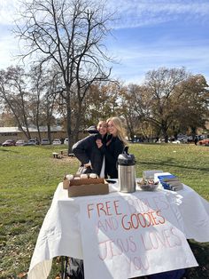 two people standing next to a sign that says free drinks and goodies jesus loves you