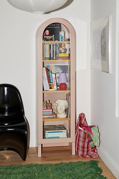 a black chair sitting in front of a book shelf next to a white wall and green rug