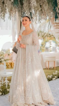 a woman in a wedding dress standing under a tree with flowers and greenery on it