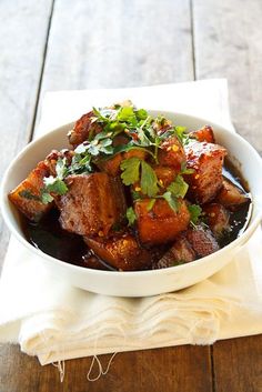 a white bowl filled with meat and garnished with cilantro on top