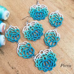 several blue and white crochet earrings on a wooden table next to spools of thread