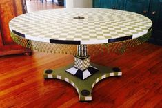 a white and black checkered table sitting on top of a hard wood floor next to a green cabinet