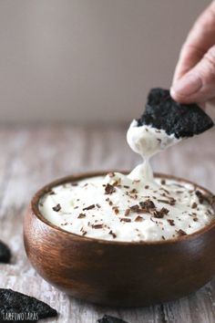 a person dipping some kind of food in a bowl with oreo chips on top