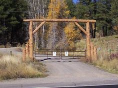 an open gate on the side of a road in front of some trees and grass