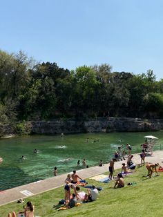 many people are swimming in the water and on the grass by the river bank,