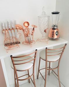 two metal chairs sitting next to each other on a white counter with copper colored accents