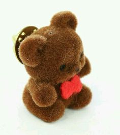 a brown teddy bear with a red heart on it's chest and a bell around its neck