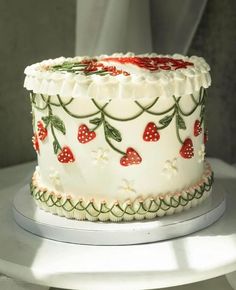 a white cake with red berries and green leaves on it