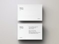 two white business cards sitting on top of each other in front of a gray wall