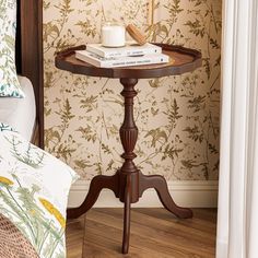 a small table with books on it in front of a floral wallpapered room