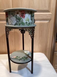 two tiered table with flowers painted on the top and one shelf holding a plate