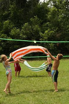 three children playing volleyball in the grass with an american flag draped over their heads and arms