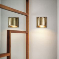 two lights on the side of a white wall next to a mirror and wooden door