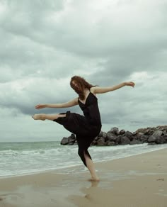 a woman standing on top of a sandy beach next to the ocean with her arms outstretched