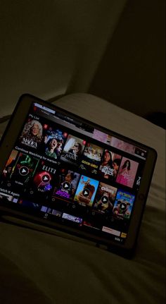 a tablet computer sitting on top of a bed next to a remote control in a dark room