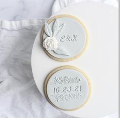 two decorated cookies sitting on top of a white cake plate with the date and number