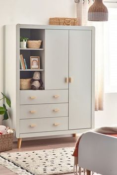 a white cabinet with drawers and shelves in a living room next to a chair, rug and potted plant