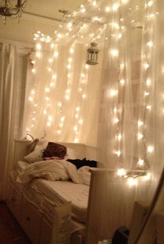 a bedroom with white lights strung from the ceiling and curtains over the bed in front of it