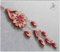 a red and gold necklace with flowers hanging from it's side on a white surface