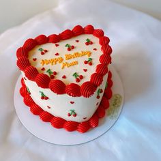 a heart shaped birthday cake on top of a white plate with red trimmings