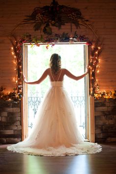 a woman standing in front of a window wearing a wedding dress and holding her arms out