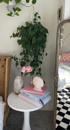 a white table topped with books and a potted plant next to a bedroom mirror