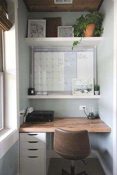 an office with a desk, chair and calendar on the wall above it is also a potted plant