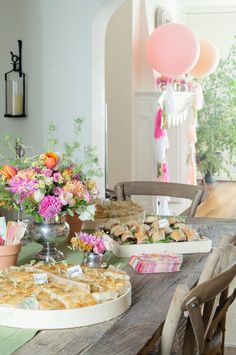 a table filled with food and flowers on top of a wooden table next to a window