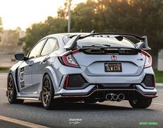 the rear end of a silver honda civic hatchback on a road with trees in the background