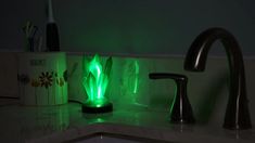 a green light shines in the dark next to a sink and toothbrush holder