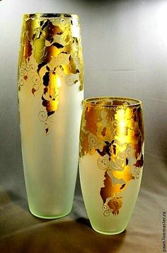 two white and gold vases sitting next to each other on a gray surface with a light behind them