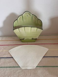 a green bowl sitting on top of a table next to a white paper napkin holder