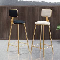 two stools with black and white upholstered seats in front of a wooden wall