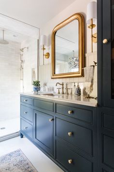 a bathroom with blue cabinets and a gold framed mirror