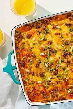 a casserole with meat, cheese and vegetables on it next to two glasses of juice