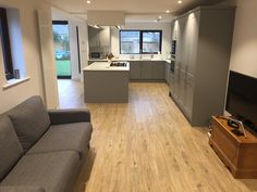 an empty living room and kitchen area in a house with wood floors, gray furniture, and large windows