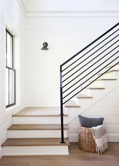 a basket is sitting on the floor next to some stairs in a house with white walls and wood floors