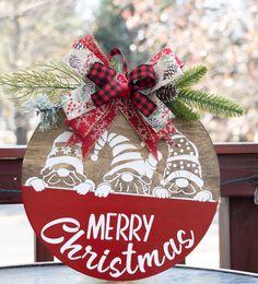 a merry christmas sign on top of a table with pine branches and red ribbon hanging from it