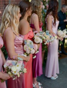 a group of women standing next to each other holding bouquets in their hands and looking at each other