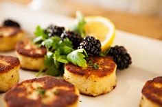 some food is sitting on a white plate with blackberries and lemons around it