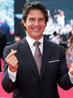 a man in a suit and tie giving the peace sign with his hand while standing on a red carpet