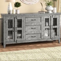 a large wooden sideboard with glass doors and drawers in a living room next to a rug